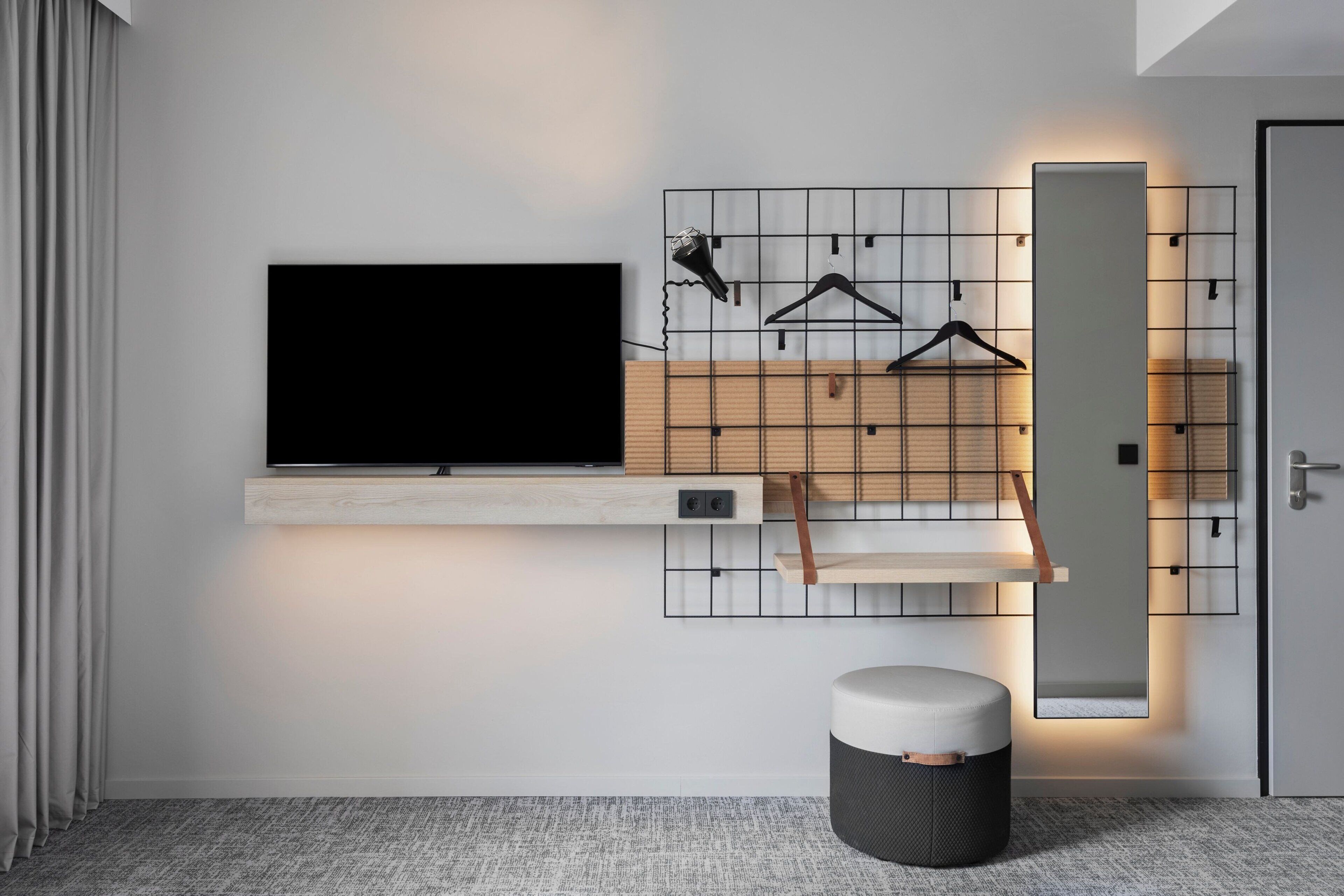 A modern living room with a mounted TV, wooden shelves, a mirror, and a small ottoman.