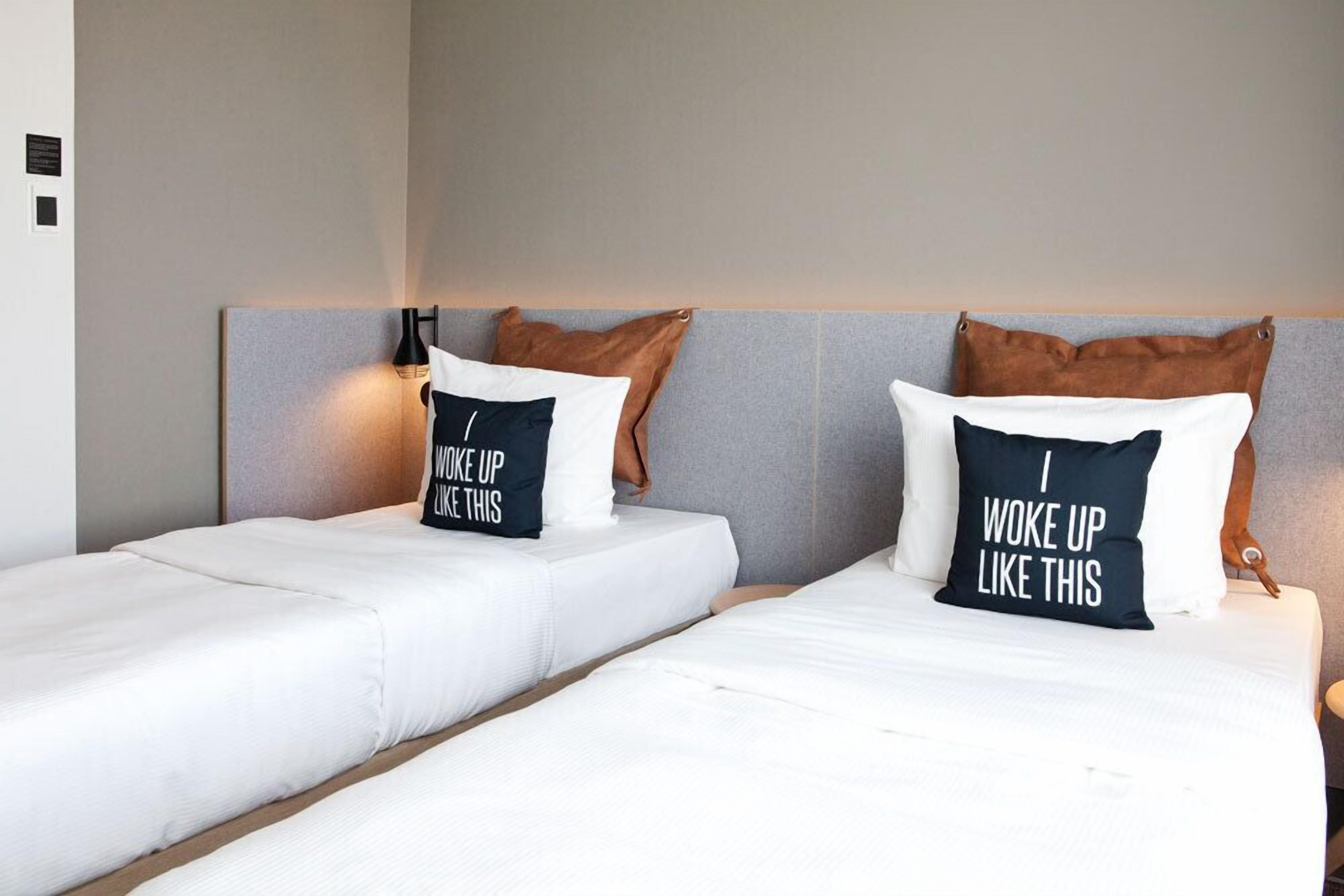 A hotel room with two beds, each with a pillow that reads "I woke up like this."
