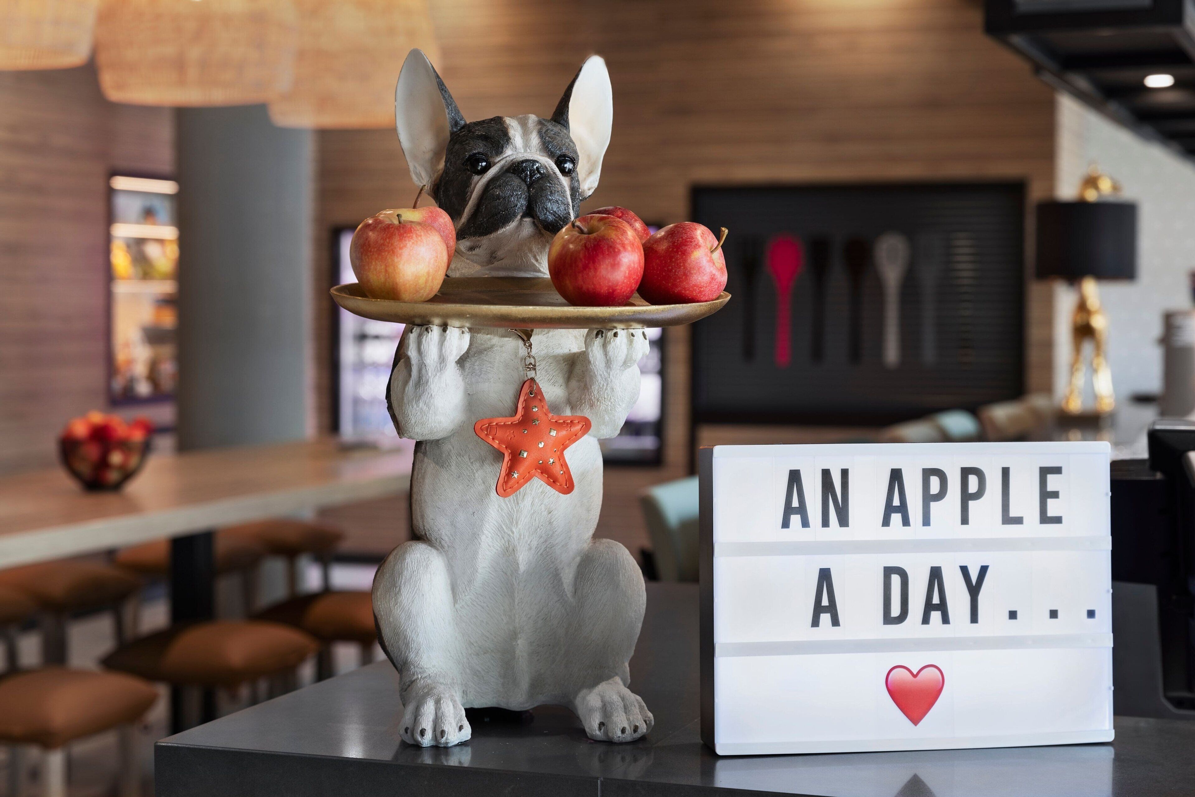 A dog figurine holding a tray with apples and a star ornament, with a sign that reads "AN APPLE A DAY...".