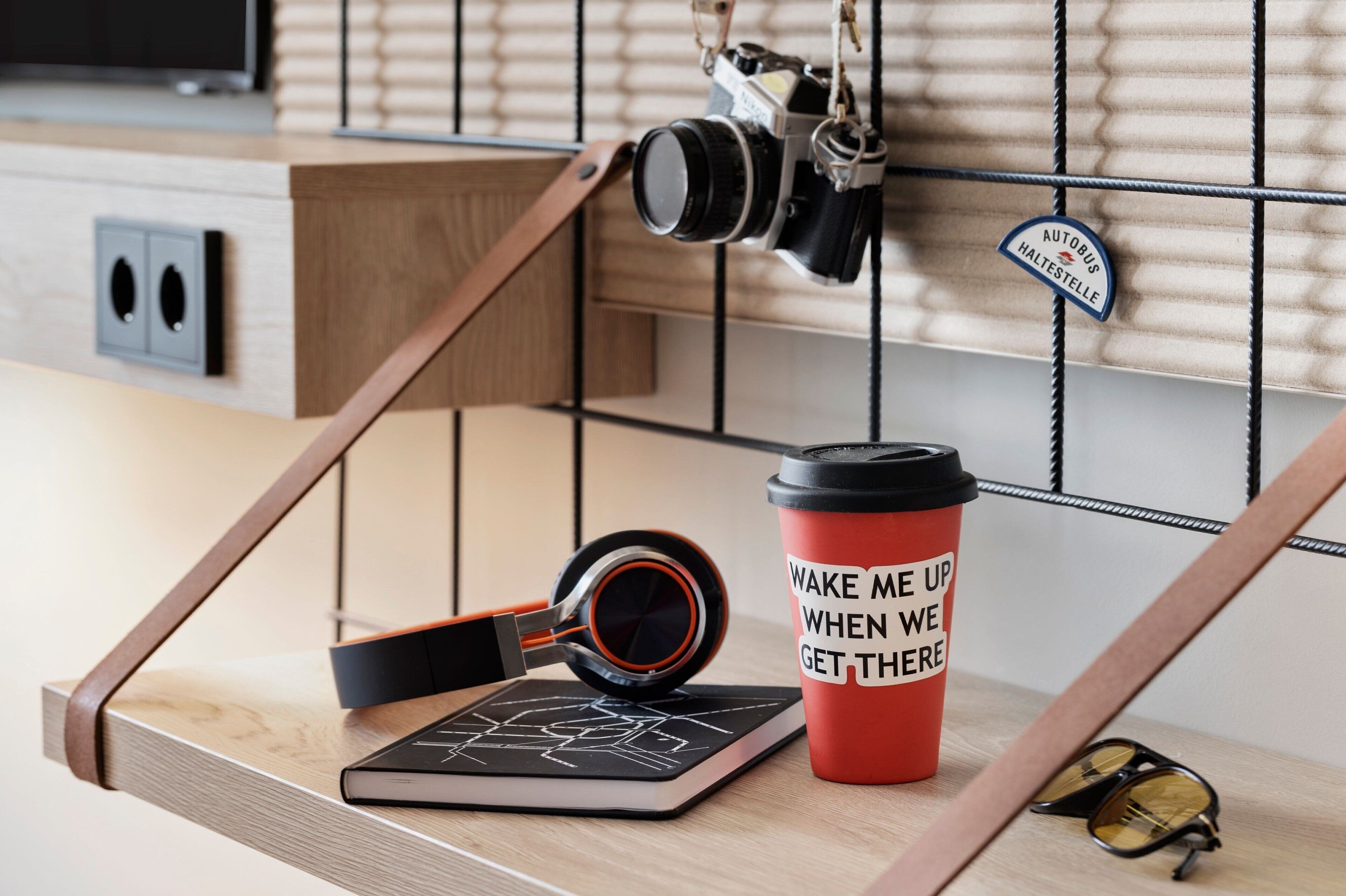 A modern kitchen with wooden cabinetry, a hanging camera, a red coffee cup with motivational text, and a pair of sunglasses on the counter.