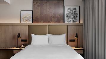 Een hotelkamer met een groot bed, twee nachtkastjes met lampen, een telefoon en een kunstwerk in een lijst aan de muur.