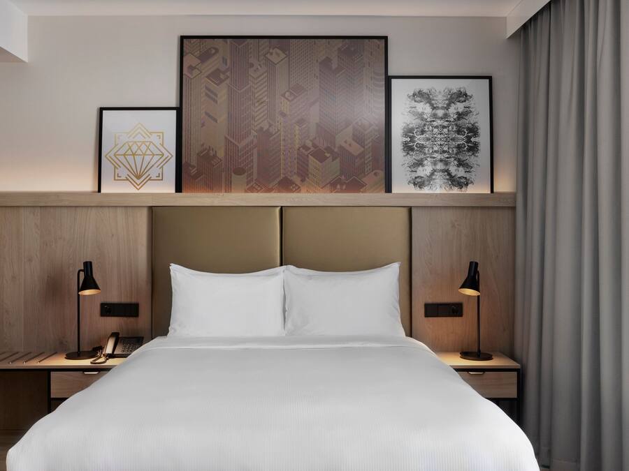Een hotelkamer met een groot bed, twee nachtkastjes met lampen, een telefoon en een kunstwerk in een lijst aan de muur.