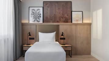 Una habitación de hotel moderna con una cama grande, cabecero de madera, dos mesitas de noche con lámparas y tres obras de arte enmarcadas sobre la cama.