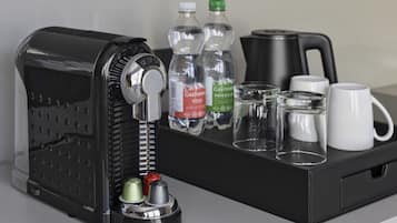 Eine Kaffeemaschine, zwei Wasserflaschen, ein Glas und zwei weiße Tassen auf einem Tablett.