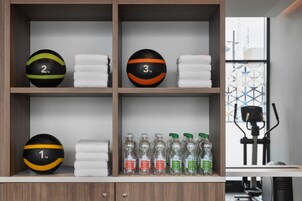 Area fitness con attrezzature per esercizi, uno scaffale con palle da ginnastica e asciugamani, e bottiglie d'acqua.