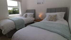 Ein Schlafzimmer mit zwei Einzelbetten, einem Nachttisch mit Lampe, einem Fenster mit Jalousien und einem Wandbild.