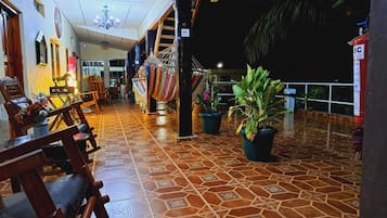 Un espacio interior amplio con suelo de baldosas, sillas de madera, plantas en macetas y una escalera que conduce a un nivel superior.