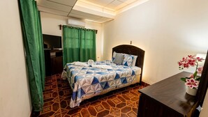 A hotel room with a bed, a desk, a TV, and a green curtain.