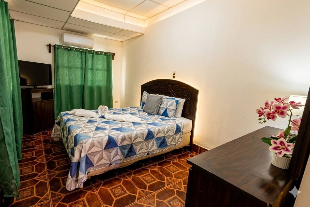 Une chambre d’hôtel avec un lit, un bureau, une télévision et un rideau vert.