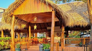 A wooden structure with a thatched roof, surrounded by potted plants and stone flooring.