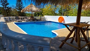 A swimming pool with lounge chairs, a thatched umbrella, and a wooden table.