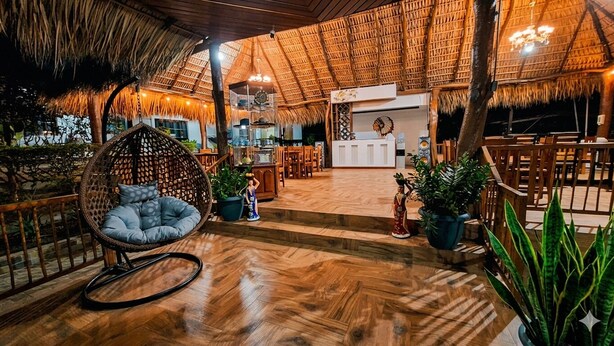 A restaurant with a thatched roof, wooden flooring, and a hanging chair.
