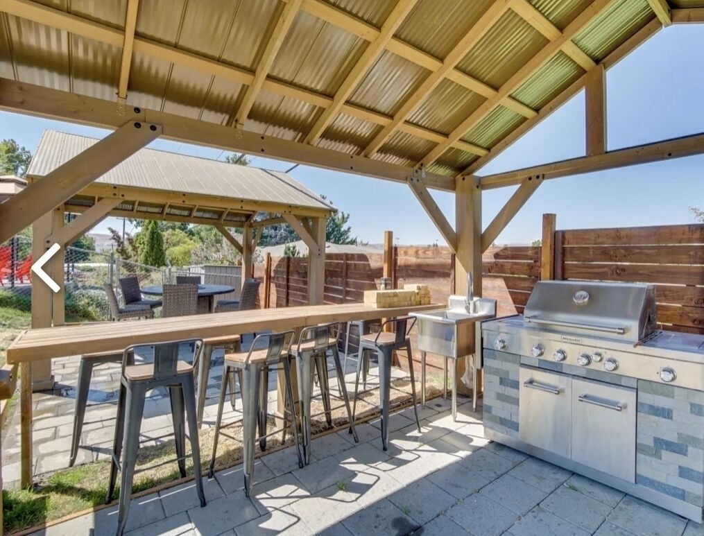 Eine Terrasse im Freien mit Grill, Barhocker und einer überdachten Sitzgelegenheit.