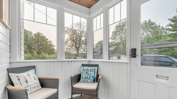 A cozy porch with wicker chairs and a cushion, large windows offering a view of the neighborhood.