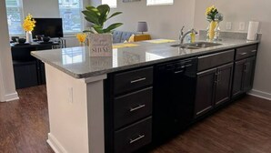 A modern kitchen with a central island, dark cabinetry, and a dining area in the background. - Serenity 1 King Bed/Pool (Moseley)