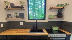 Una cocina moderna con encimera de madera, armarios negros, un lavamanos, una estufa y una ventana con vistas a árboles.