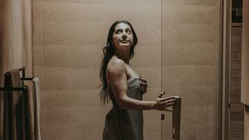 A woman in a bathroom with a towel rack, a showerhead, and a small table with bottles.