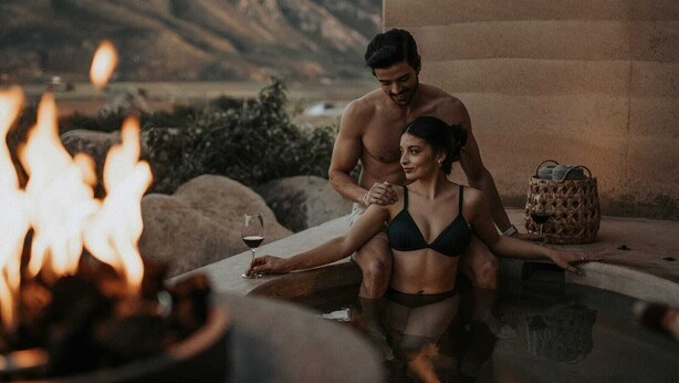 A couple in a hot tub with a mountain view, a fire, and a woven basket. - MIRA Earth Studios (Valle de Guadalupe)