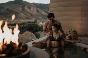 A couple in a hot tub with a mountain view, a fire, and a woven basket. - MIRA Earth Studios (Valle de Guadalupe)