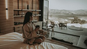 A person sitting on a bed in a modern room with a large window overlooking a snowy landscape. - MIRA Earth Studios (Valle de Guadalupe)