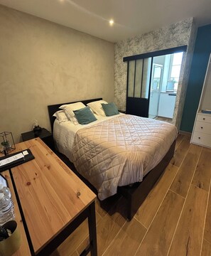 Un dormitorio con una cama, una mesa de madera, una mesita de noche y una ventana con vistas.