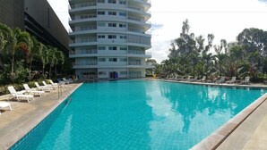 Una piscina con sillas de descanso, un edificio de varios pisos y vegetación tropical.