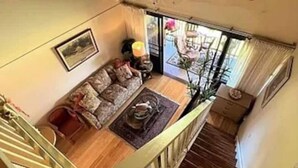 A room with a sofa, a small table, a staircase, and a view of the outdoors. - 1-bedroom condo in Maunaloa, just 10 minutes from the beach (Maunaloa)