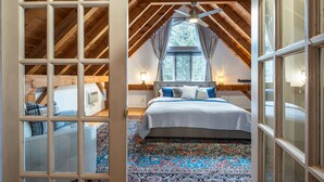 A bedroom with a sloped ceiling, a large bed with a patterned rug, and a window with curtains. - Maison Napoleon (Mont-Tremblant)