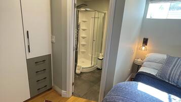 A bedroom with a bed, a nightstand, a window, and a bathroom visible through an open door.