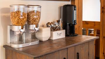 Una barra de desayuno con dispensadores de cereales, una cafetera y un cartel que dice 'Bon appétit'.