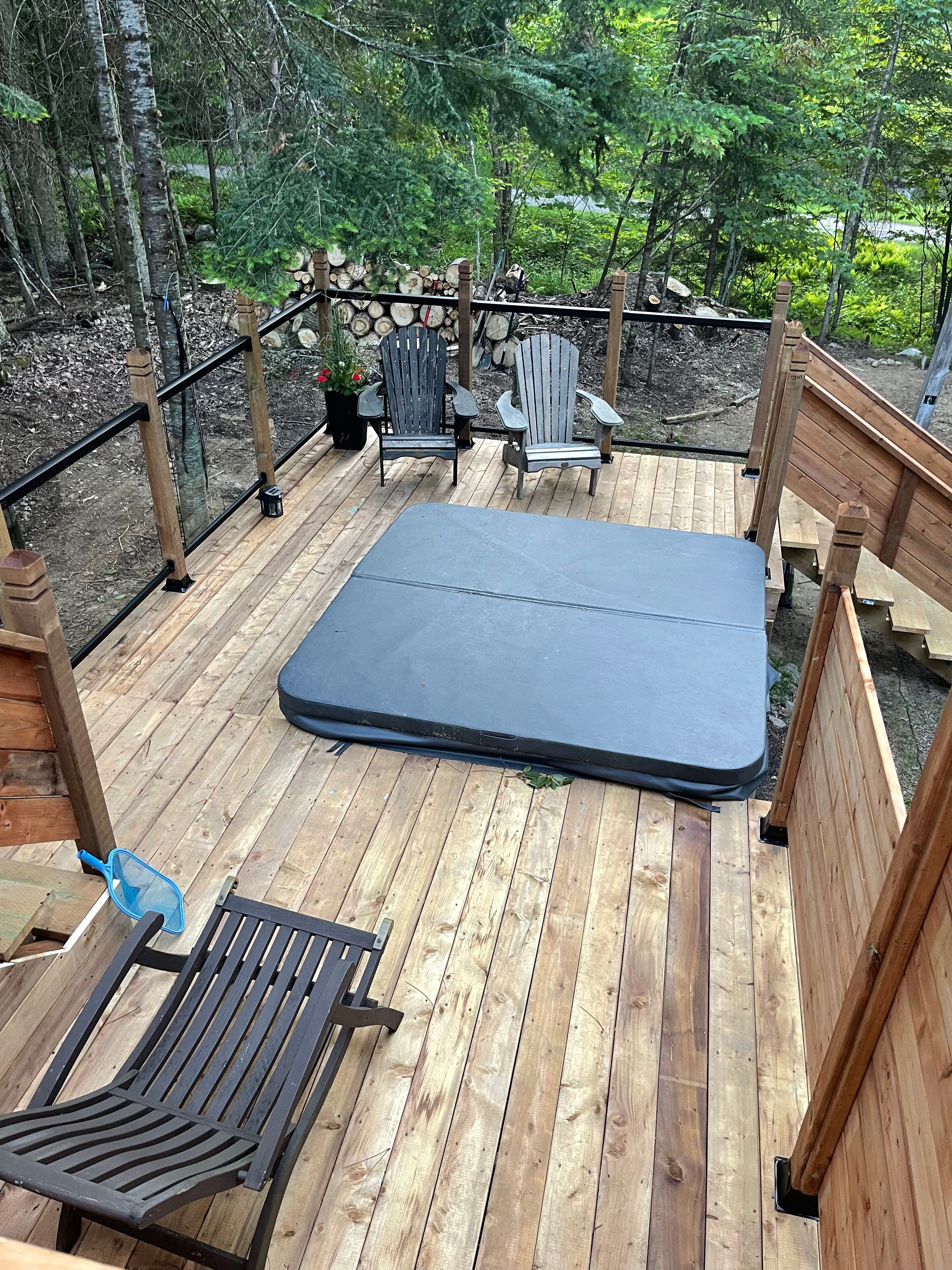 Una terraza de madera con un colchón, dos sillas Adirondack y una red azul.
