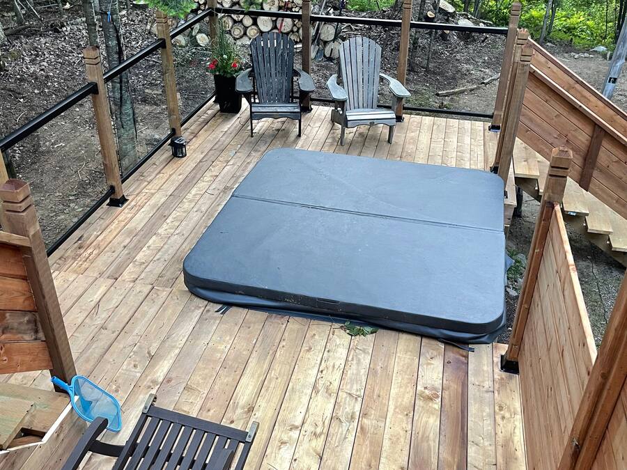 Um deck de madeira com um colchão, duas cadeiras Adirondack e uma rede azul.