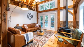 A cozy living room with a wooden ceiling, a large window, a fireplace, and a leather sofa. - Maison Napoleon (Mont-Tremblant)
