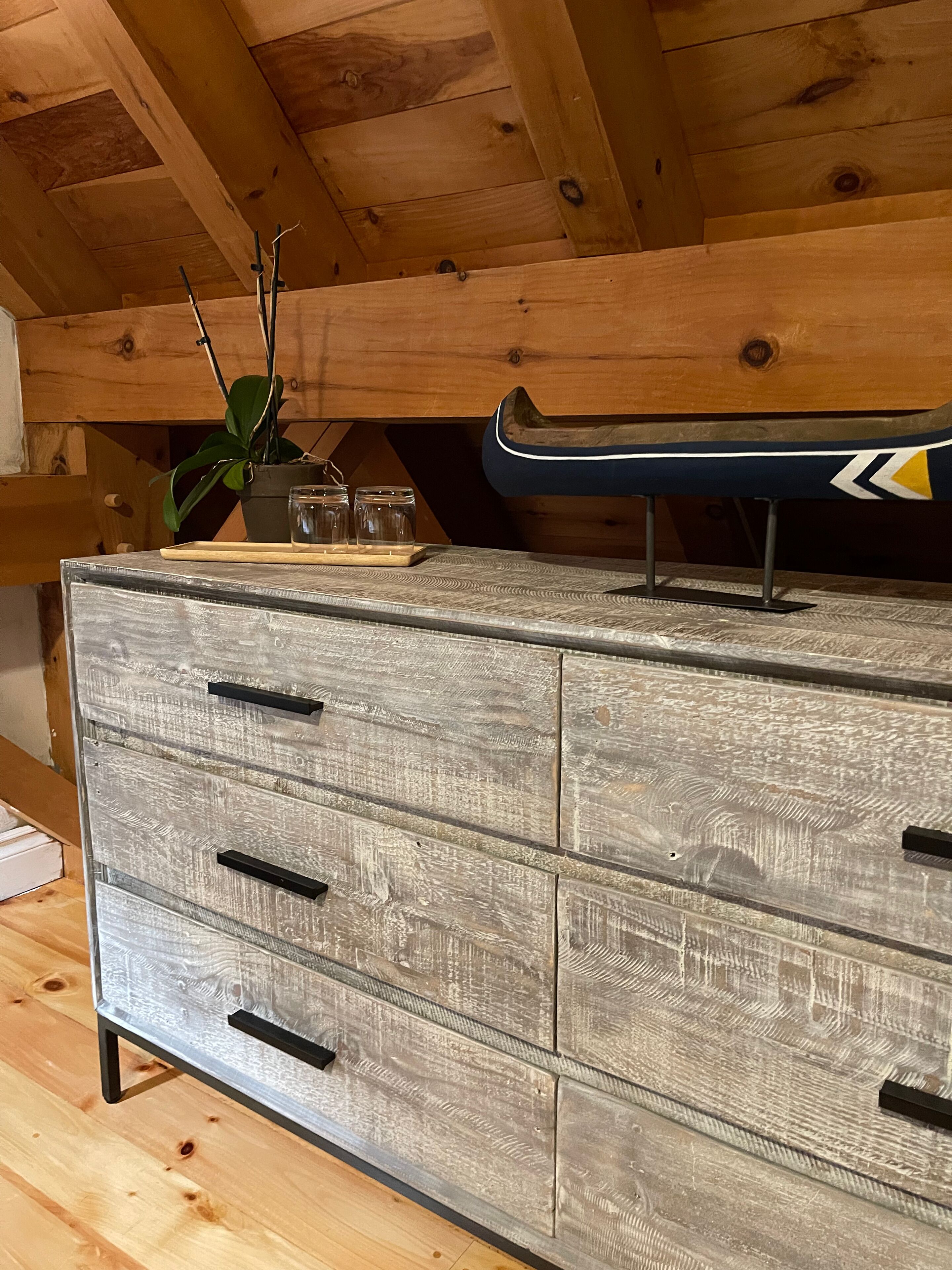 A wooden ceiling with exposed beams, a wooden dresser with drawers, and a plant on top.