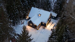 A snow-covered house with a sloped roof, a chimney, and a deck with outdoor seating. - Maison Napoleon (Mont-Tremblant)