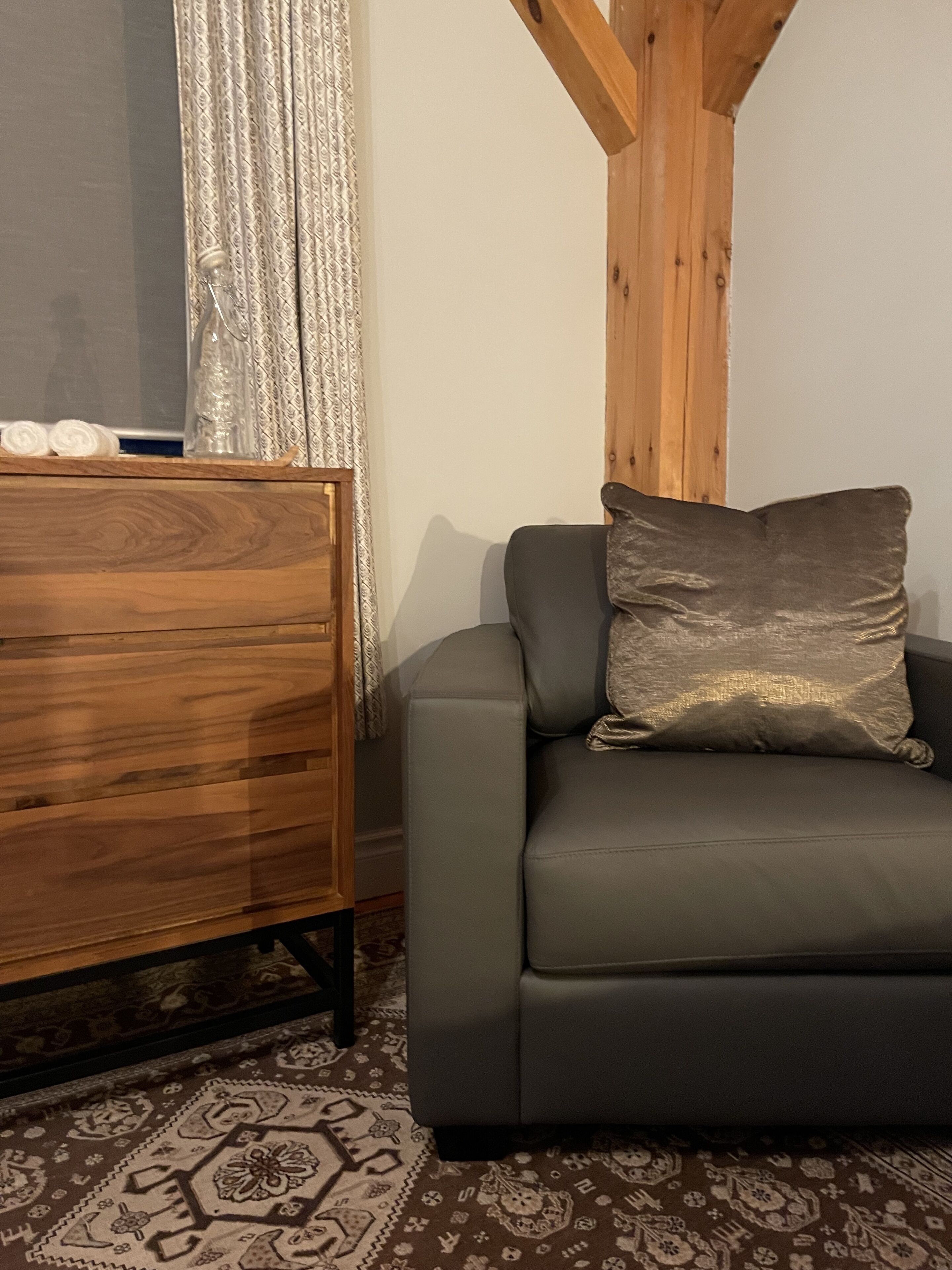 A grey sofa with a textured cushion, a wooden dresser, and a patterned rug.