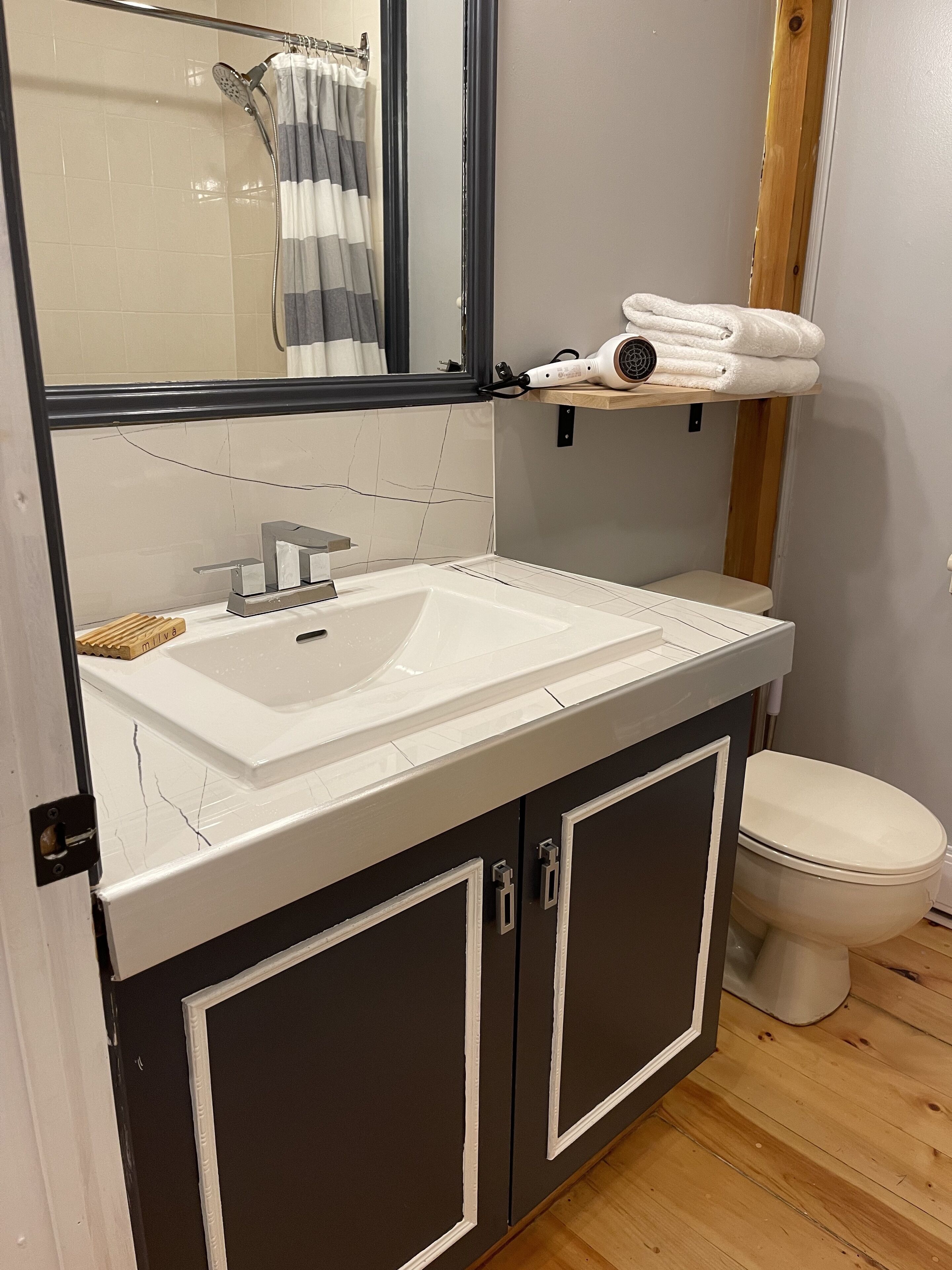 Une salle de bain avec un lavabo blanc, des meubles sombres, des toilettes et un porte-serviettes avec des serviettes.
