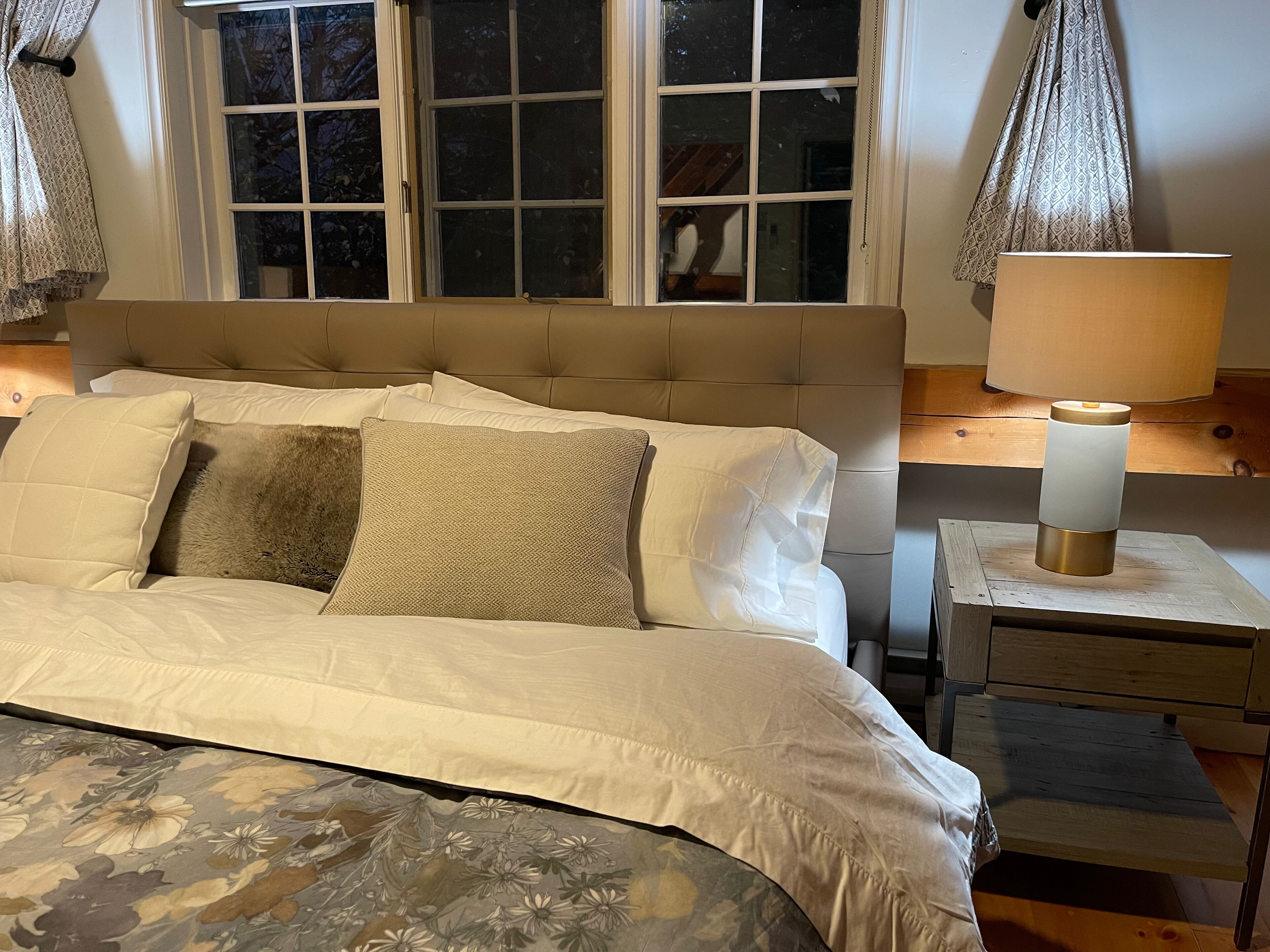 Un dormitorio con cama, mesita de noche, lámpara y ventana con cortinas.