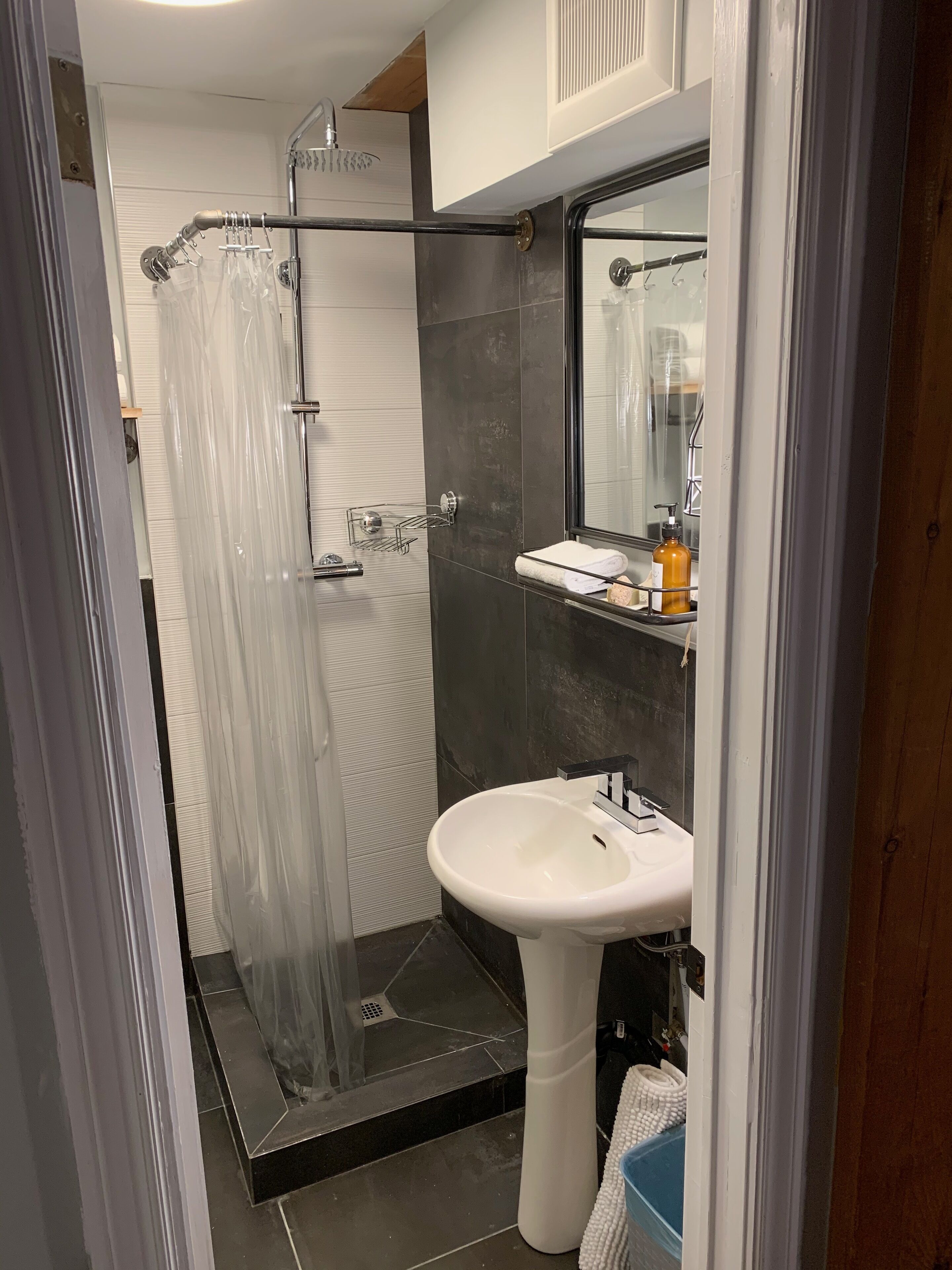 Un baño moderno con cabina de ducha de vidrio, un lavabo pedestal y un espejo sobre el lavabo.