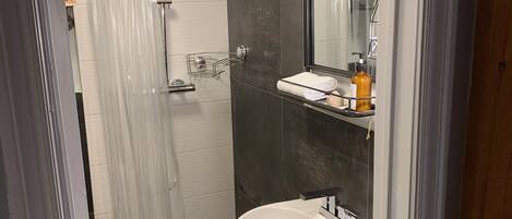 Un baño moderno con cabina de ducha de vidrio, un lavabo pedestal y un espejo sobre el lavabo.