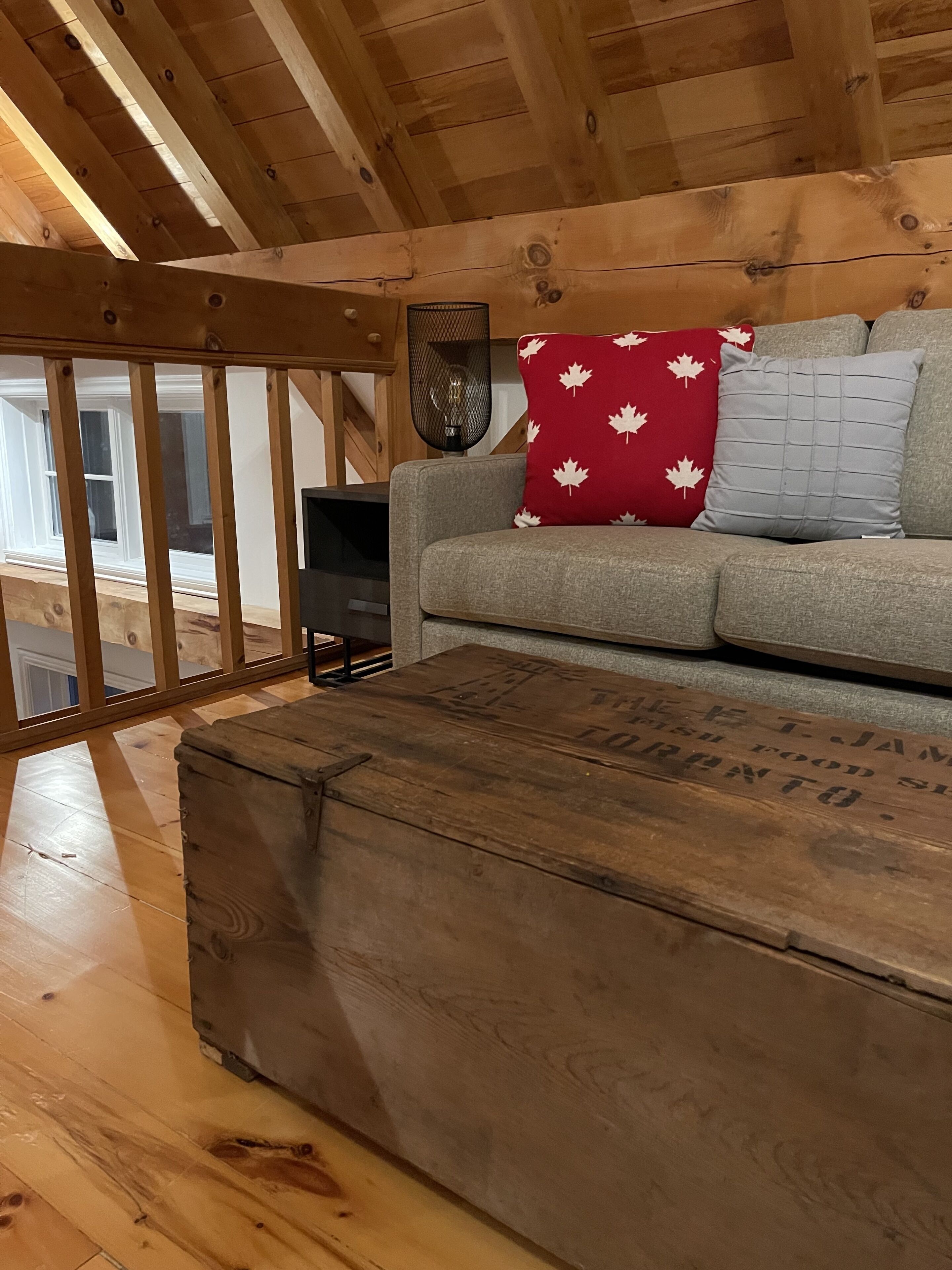 A cozy room with a wooden ceiling, a grey sofa with patterned cushions, and a vintage wooden chest.