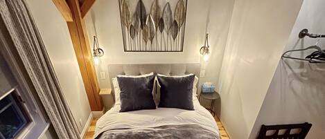 Un dormitorio con cama, mesita de noche, lámpara, ventana y puerta.