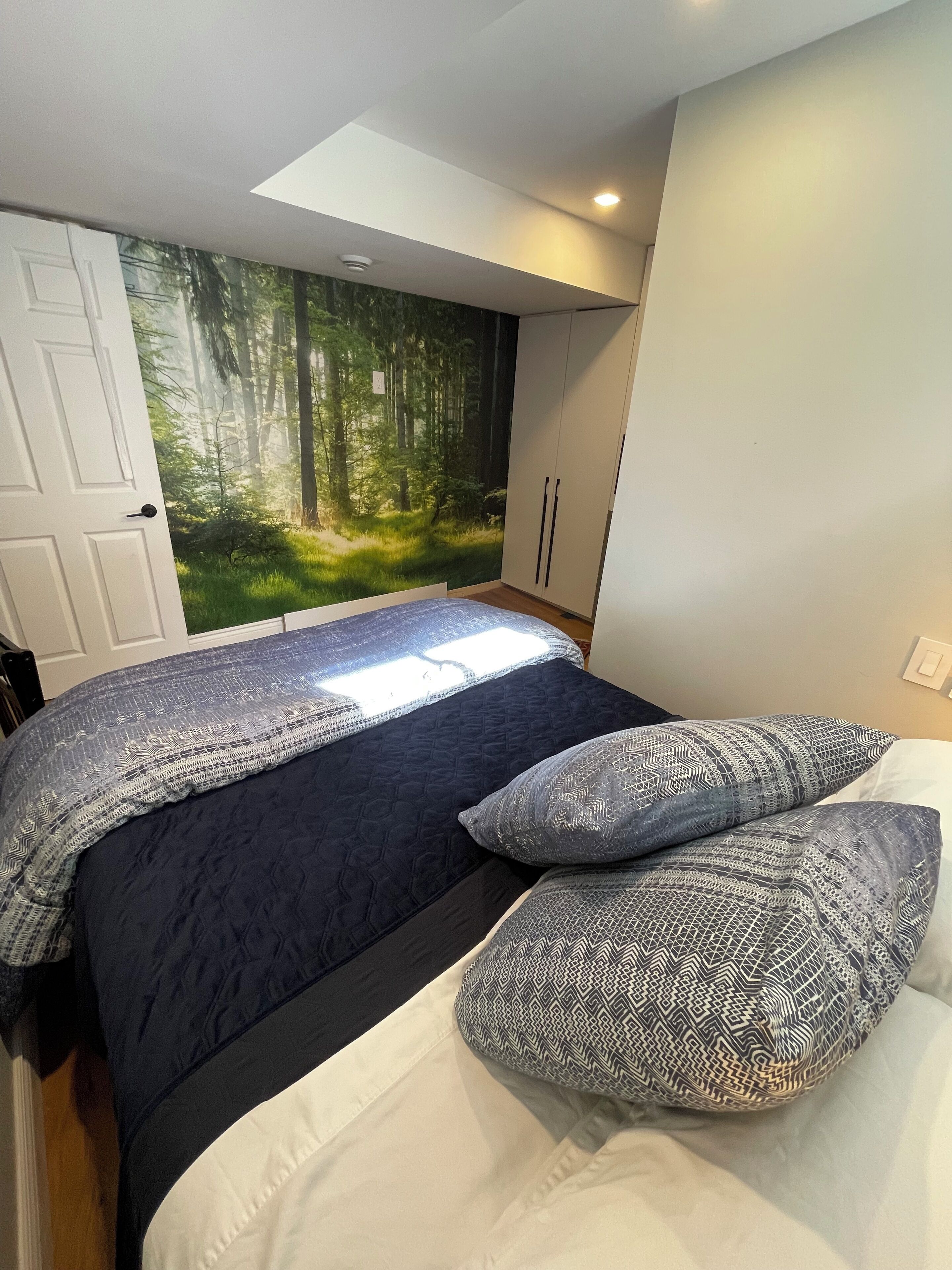 A bedroom with a large bed, a forest mural on the wall, and a skylight.