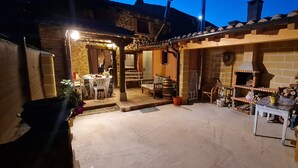 Un espacio comedor rústico al aire libre con un horno de ladrillo, muebles de madera y una pared de piedra.