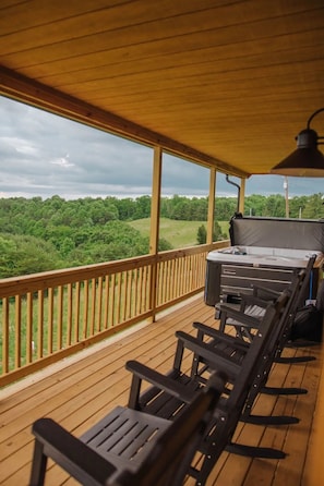 Une terrasse extérieure couverte avec un plancher en bois, un jacuzzi et des chaises noires.