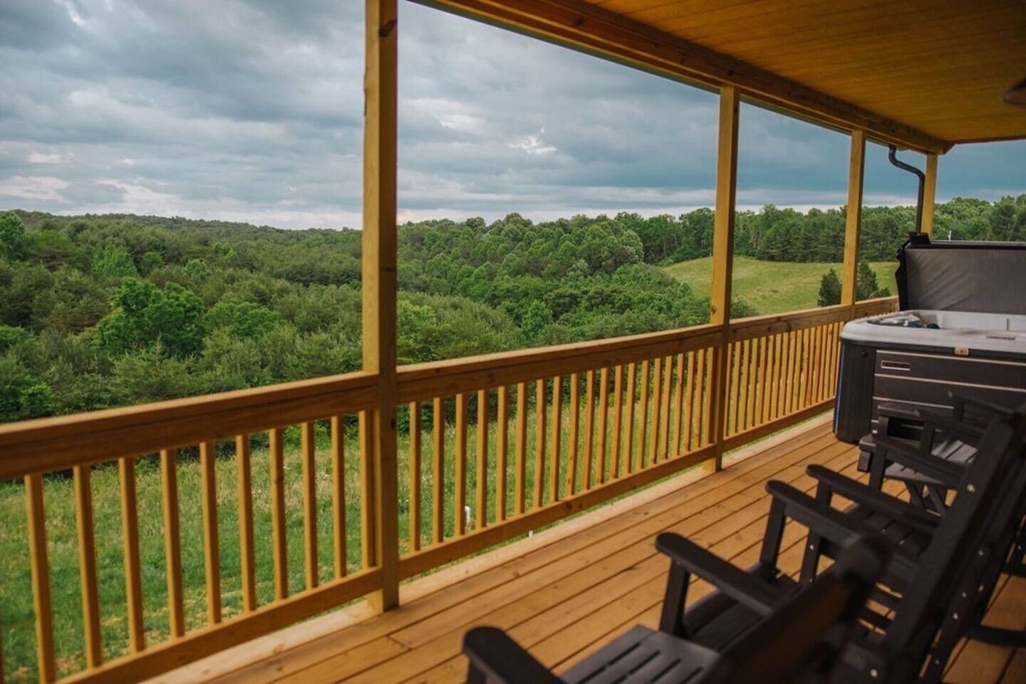 A wooden deck with a grill and chairs, overlooking a forested landscape.