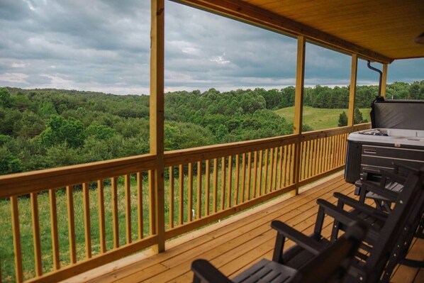 A wooden deck with a grill and chairs, overlooking a forested landscape.