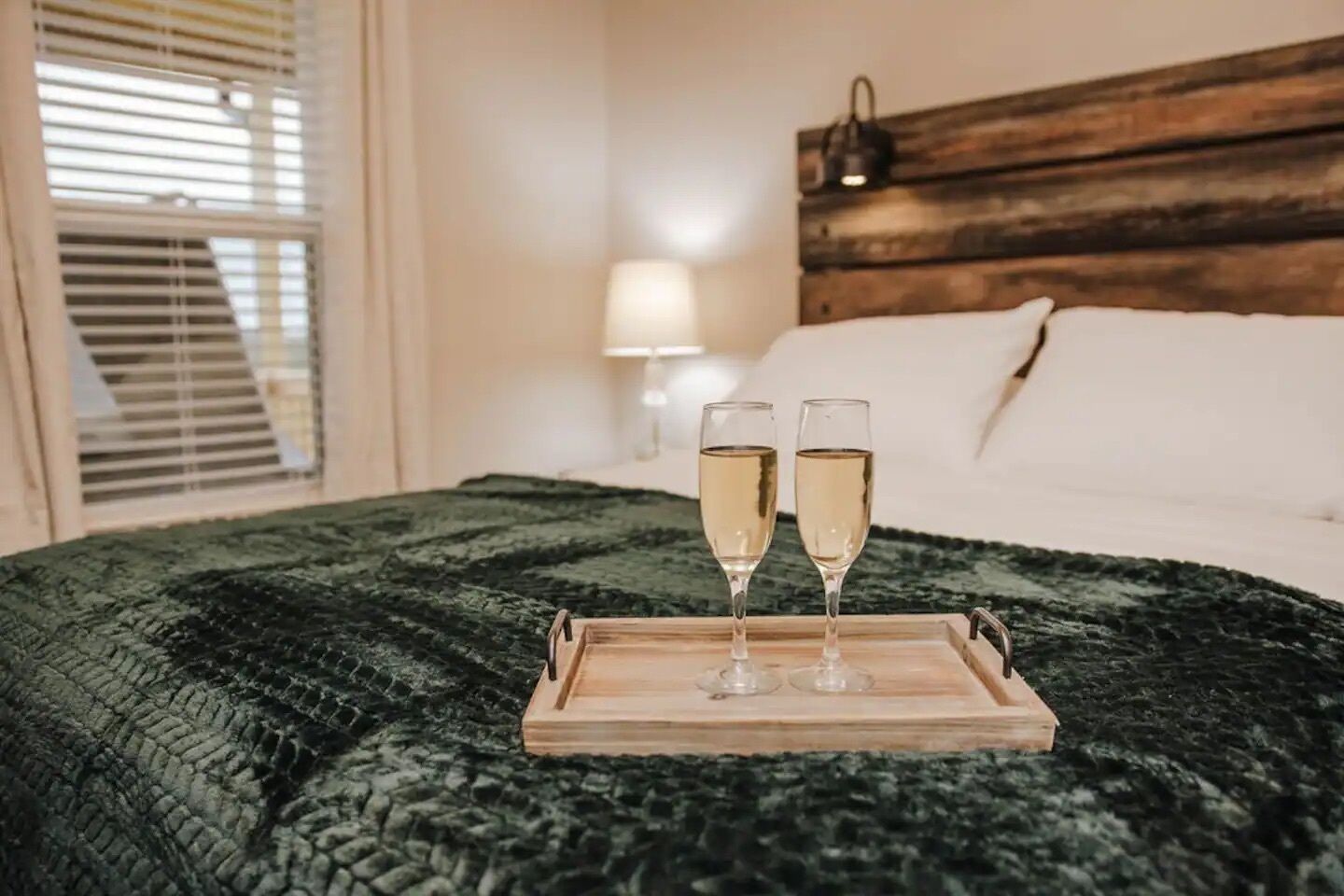 Un lit avec une tête de lit en bois, une lampe de chevet et un plateau avec deux coupes de champagne.