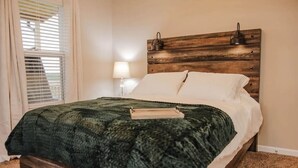 A bedroom with a wooden headboard, a green textured bedspread, white pillows, and a bedside lamp.