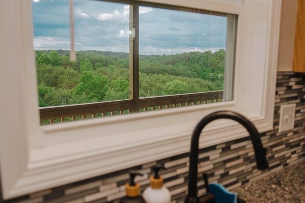 Uma cozinha com janela dando vista para uma área arborizada.